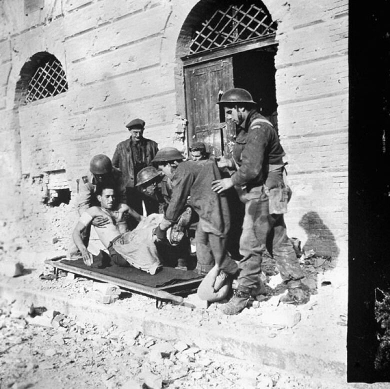 Canadian first-aid personnel place an injured soldier on a stretcher in a black and white photo from Ortona, Italy, on Dec. 21, 1943.