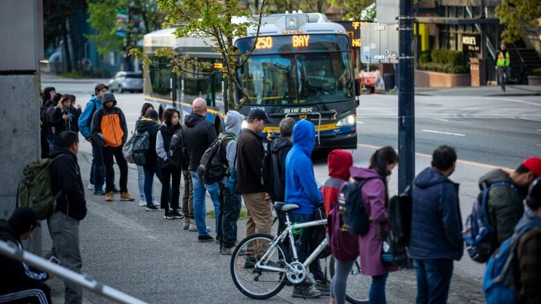 A line of transit riders wait for a bus marked '250 BAY' in a city.