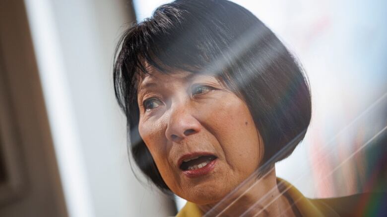 A woman is seen with shards of light shining over her face through a window.