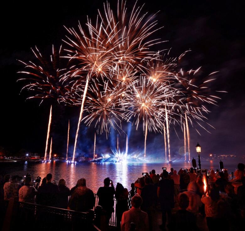 People gather around a lagoon as they watch a brilliant fireworks display in bright blue and yellow colours.