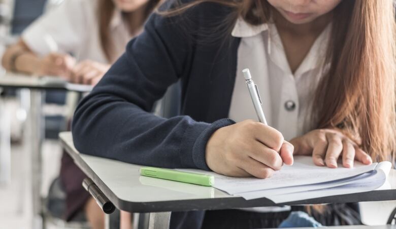 Student hand holding pen writing doing examination with blurred abstract background university students in uniform attending exam classroom educational school