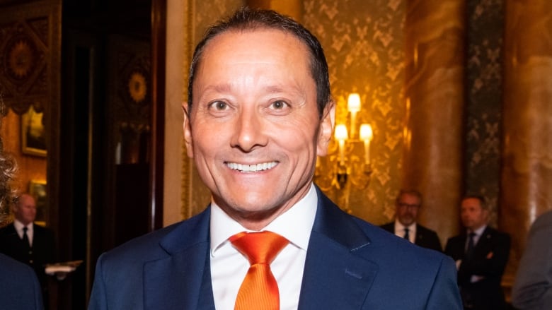 An image of a smiling man in a suit and orange tie