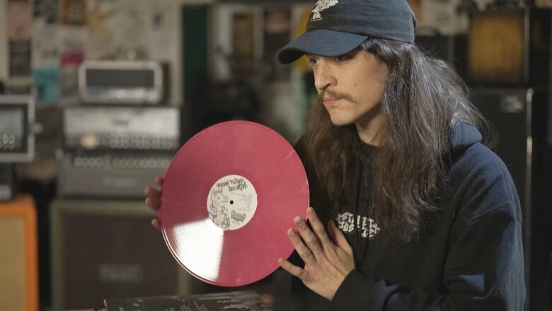 A man with long hair and a mustache holds up a vinyl record.