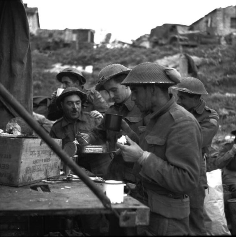 A black and white photo shows Canadian soldiers having tea and sandwiches in the town of Ortona, Italy, on Dec. 21, 1943.