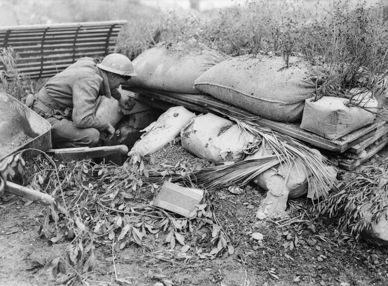 A black and white photo shows a Canadian soldier inspecting a German machine gun nest on Jan. 14, 1944, following the capture of Ortona, Italy.