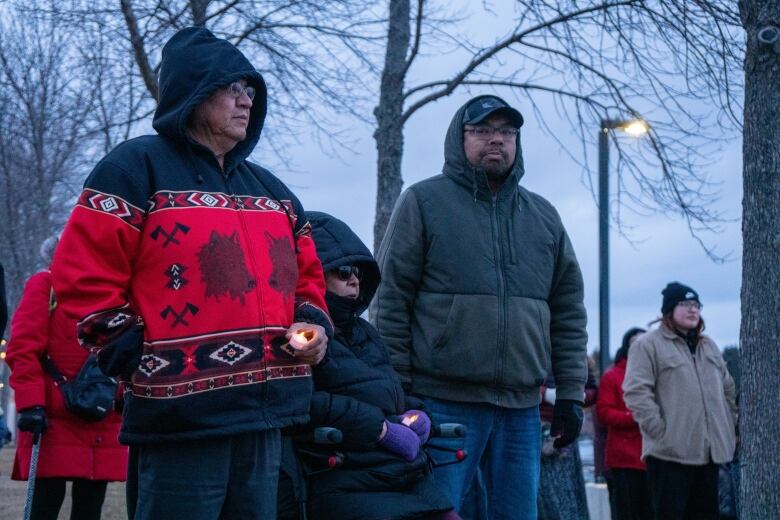 People are seen standing outside, holding tealight candles.