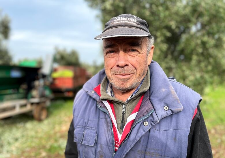 An elderly man in a cap by an olive tree.