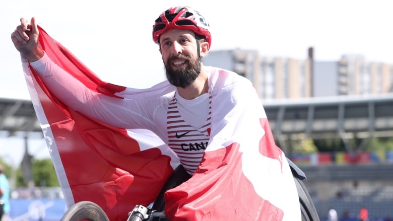 A wheelchair racer drapes a Canadian flag over his shoulders in celebration.