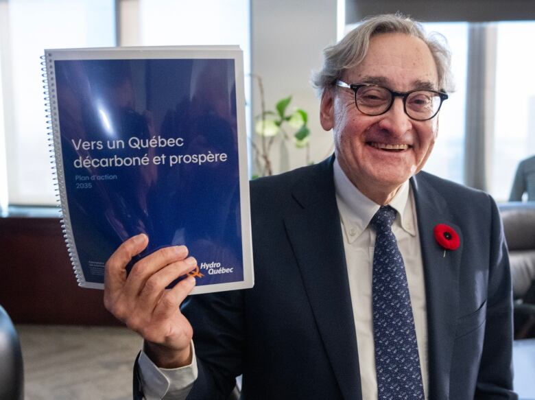 A smiling man in a suit holds up a report with French writing on the cover.