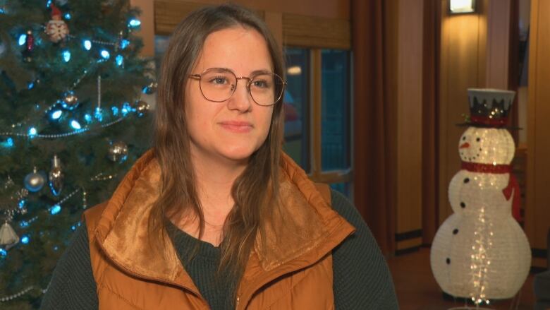 A woman talks to a reporter with a Christmas tree and snowman in the background.