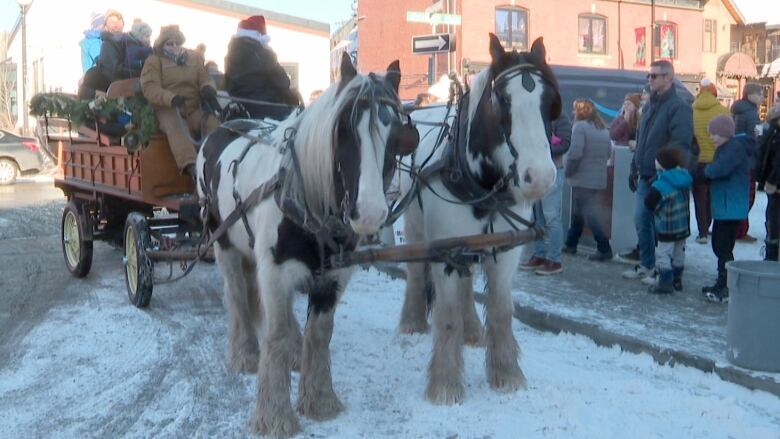 Two horses pull a wagon along a snowy city street.