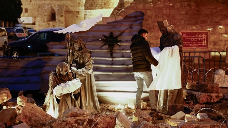 A man walks through the nativity scene setup in Bethlehem's Manger Square, surrounded by rubble and razor wire.