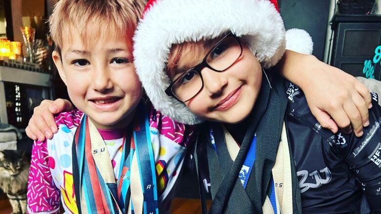 Two boys, one with a Santa hat wear many medals around their necks.