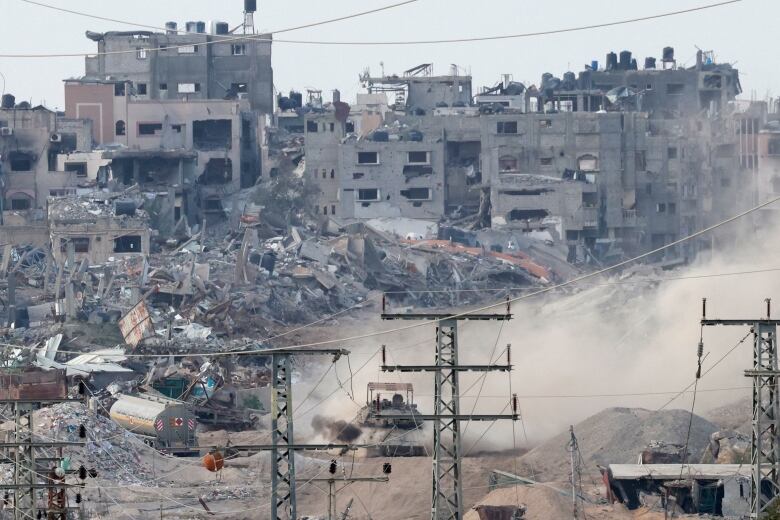 A tank drives through a city with destroyed buildings.