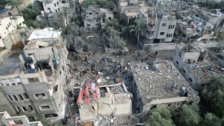 Several demolished buildings are shown from overhead with people gathered around the rubble.