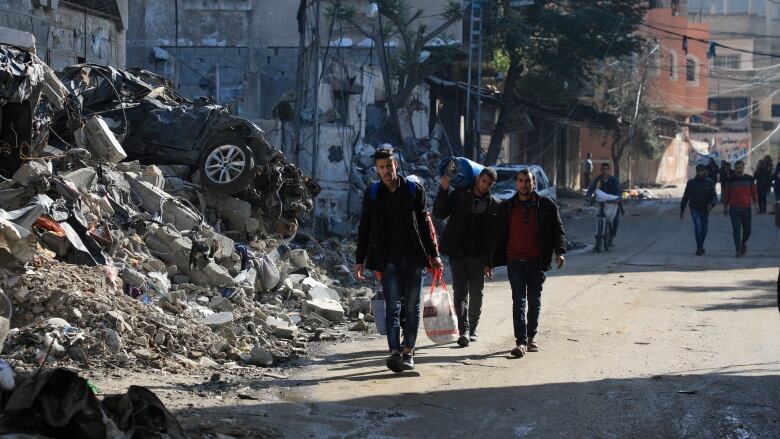 Three men holding various belongings walk by a pile of rubble.