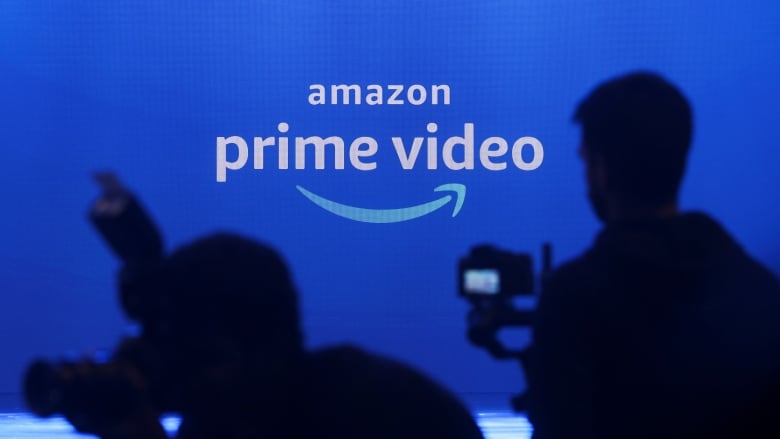 Two cameramen are silhouetted in front of a blue Amazon Prime Video logo.