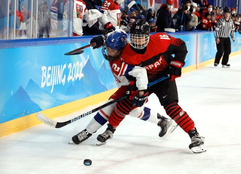 two hockey players jockey for a puck.