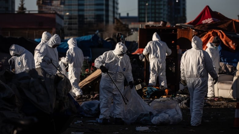 People in white suits move among belongings.