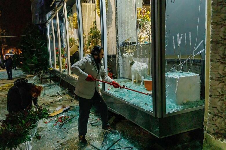 A man clears broken glass in a storefront.