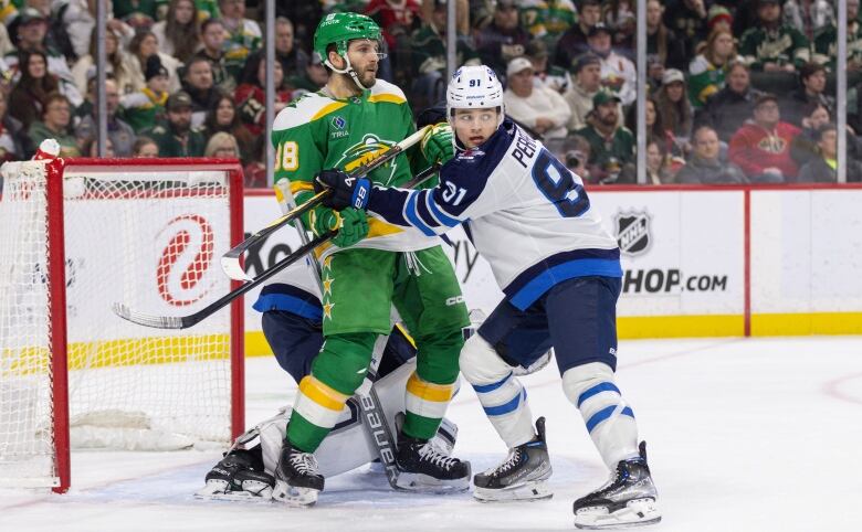 Two hockey players jockey for position in front of the goal.