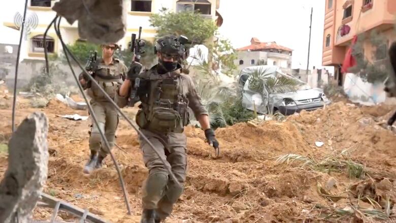 Two Israeli soldiers walk with guns drawn.