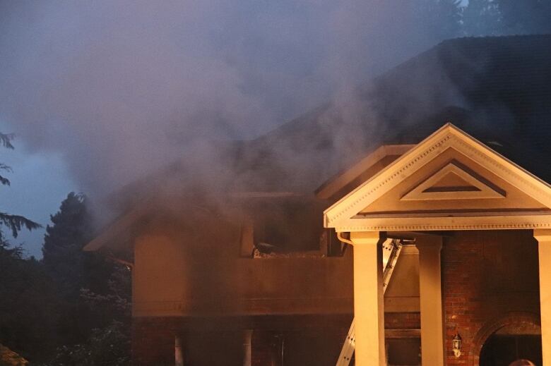 Smoke billows out of a home's second story window.