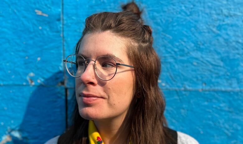 A woman with her hair in a half-up half down hairstyle looks left against a blue wall. 