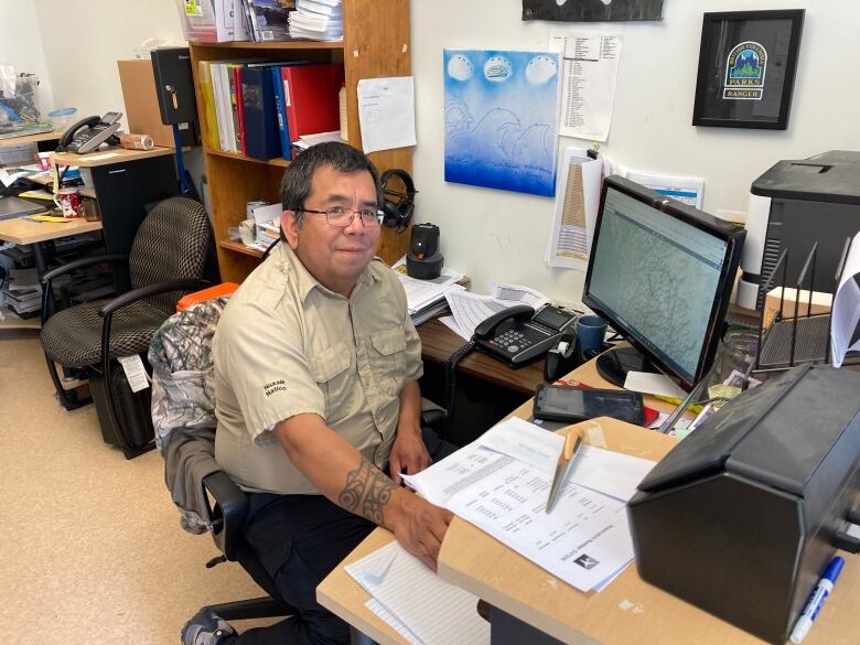 A man sits at a desk behind a computer. 