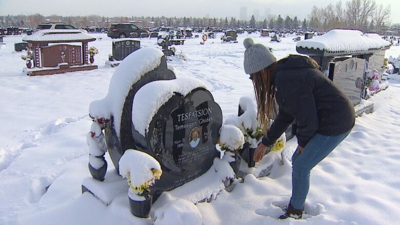 A woman bends down beside a gravestone in a cemetery in Calgary. 