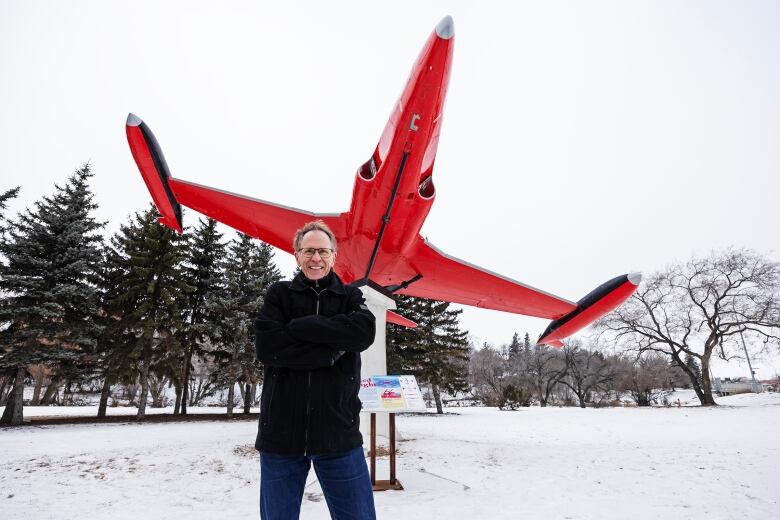 A man stands in a snowy field in front of a monument featuring a small red airplane.