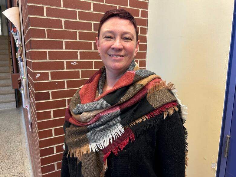 A woman in a black top and a colourful scarf stands in a university hallway.