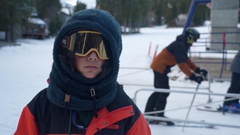 A boy in ski googles in front of a chairlift. 