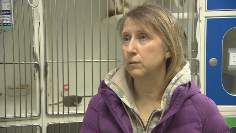 A woman stands in front of a cage with a cat inside.