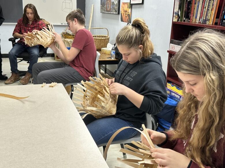 Four teenagers sit in a classroom weaving baskets.