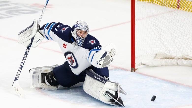 A hockey goalie does the splits and reaches out with his glove to make a save.