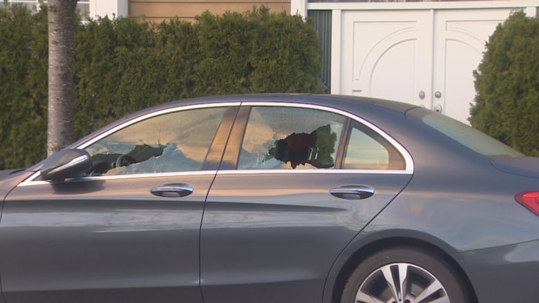 A blue sedan car with its windows smashed lies parked in front of a house.