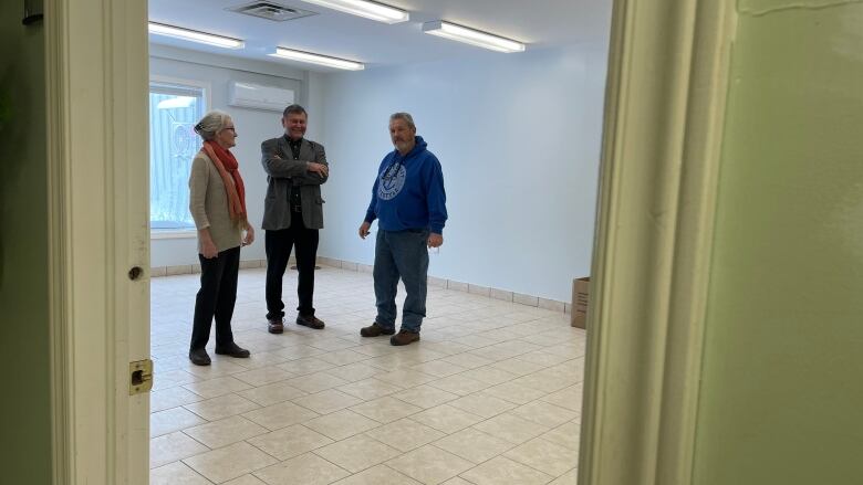 Three people, two men and one woman, stand in a vacant room in a shopping mall.