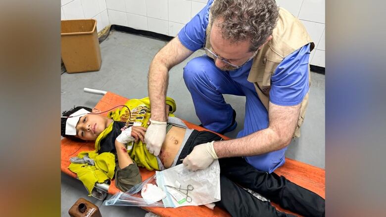 man in scrubs kneels over child laying on stretcher