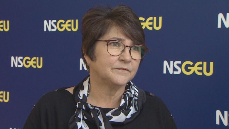 A woman with short dark hair and glasses stands in front of a baner that says NSGEU.