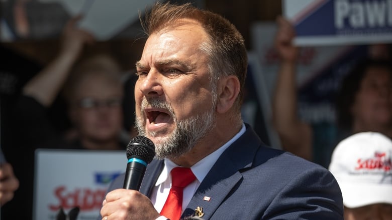 A man with a microphone speaks in front of a crowd.