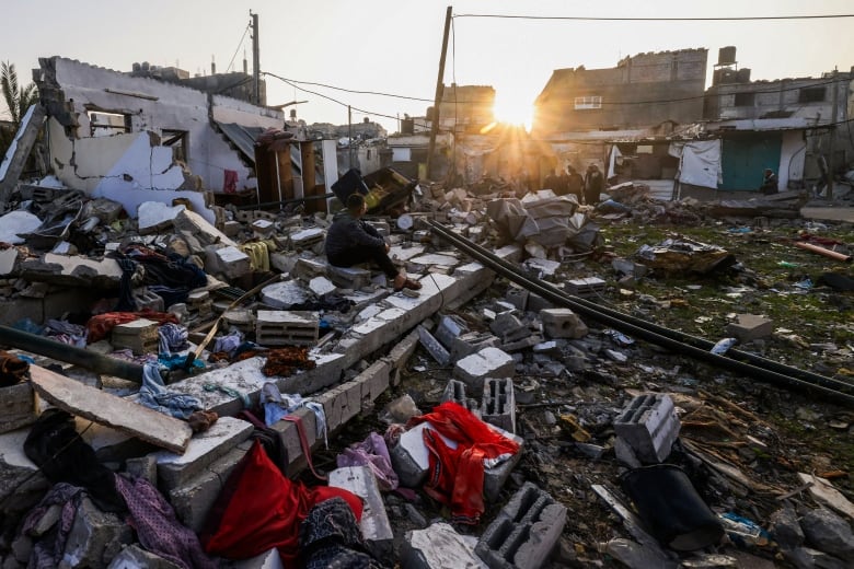 A boy sits on the rubble of a destroyed building.