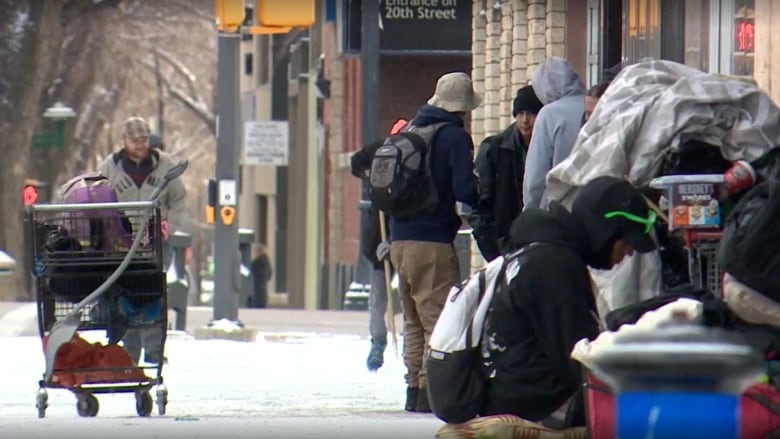 A group of people huddle on the sidewalk in the winter snow 