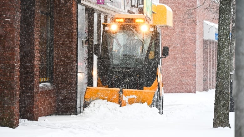 A small plow on a sidewalk pushing snow