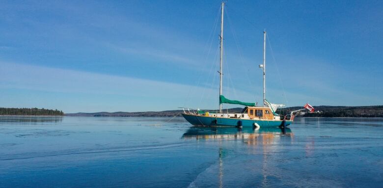 A double-masted sailboat is frozen into the ice on a body of water. 