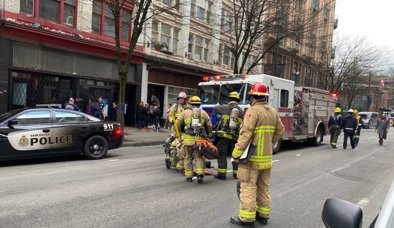 Several firefighters congregate in front of a fire truck. A police car is also on the street.