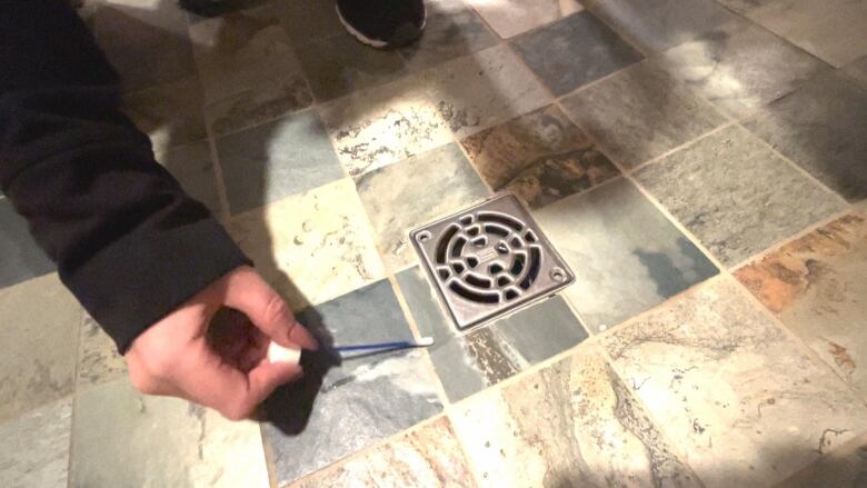 A hand holding a swab next to a shower drain