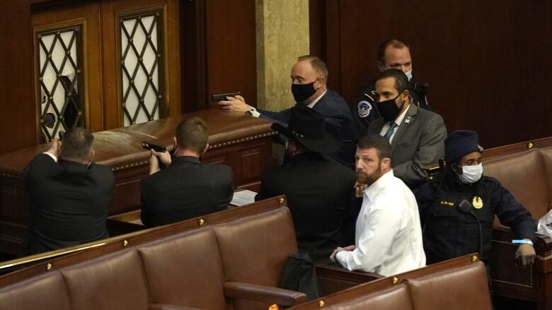 Men in dark jackets point their guns toward the door while inside a legislative chamber.