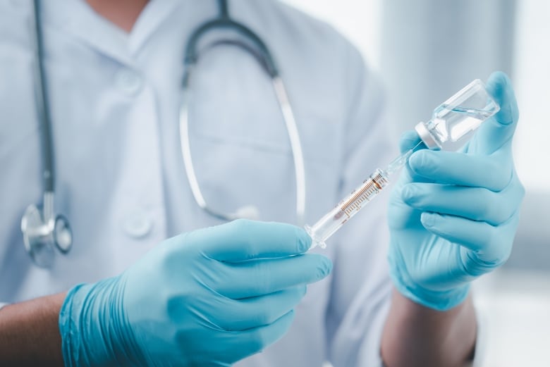 A photo of a medical worker with a stethoscope holding up a syringe going into a bottle.