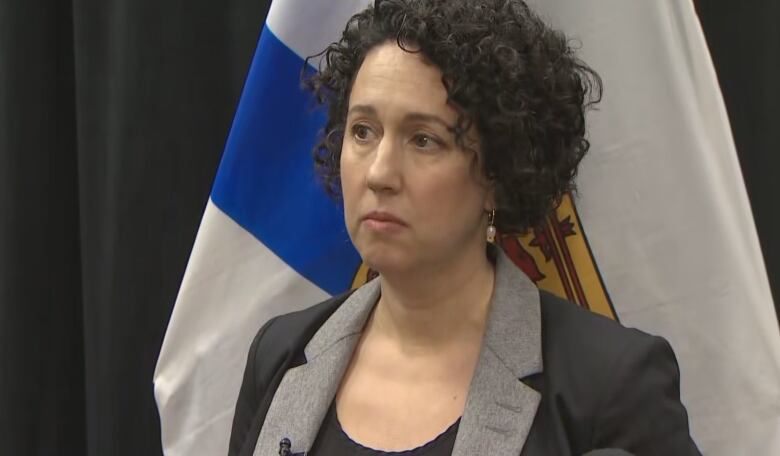 A woman with dark hair stands in front of a Nova Scotia flag.